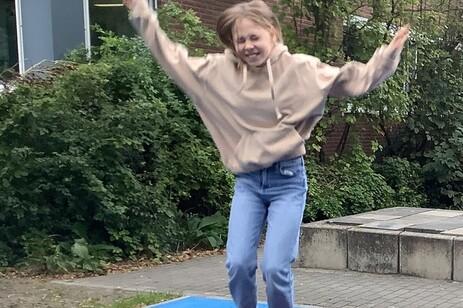 Mädchen springt fröhlich auf einem blauen Trampolin mit rotem Sprungbereich in einem Spielplatz.