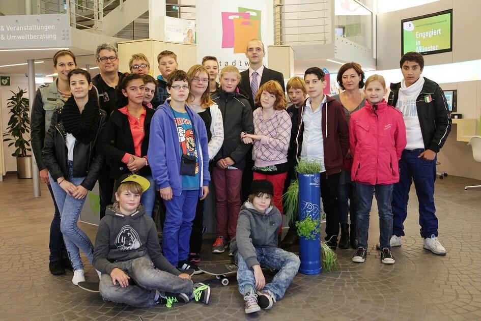 Gruppe von Jugendlichen und Erwachsenen posiert in einem modernen Innenraum mit Pflanzen und Informationsst&auml;nden.