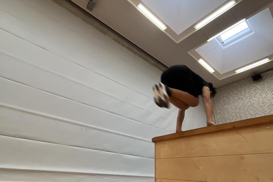 Turner f&uuml;hrt einen Handstand &uuml;ber eine Holzkastenbank in einer Sporthalle mit Oberlichtern durch.