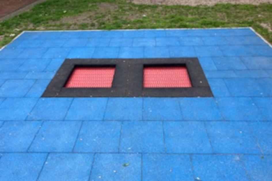 Blaue Spielplatzfl&auml;che mit zwei schwarzen &Ouml;ffnungen, darunter rote Gitterstrukturen.