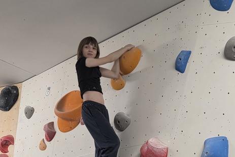 Mädchen klettert an einer Bouldering-Wand mit bunten Griffen in einem Kletterraum.